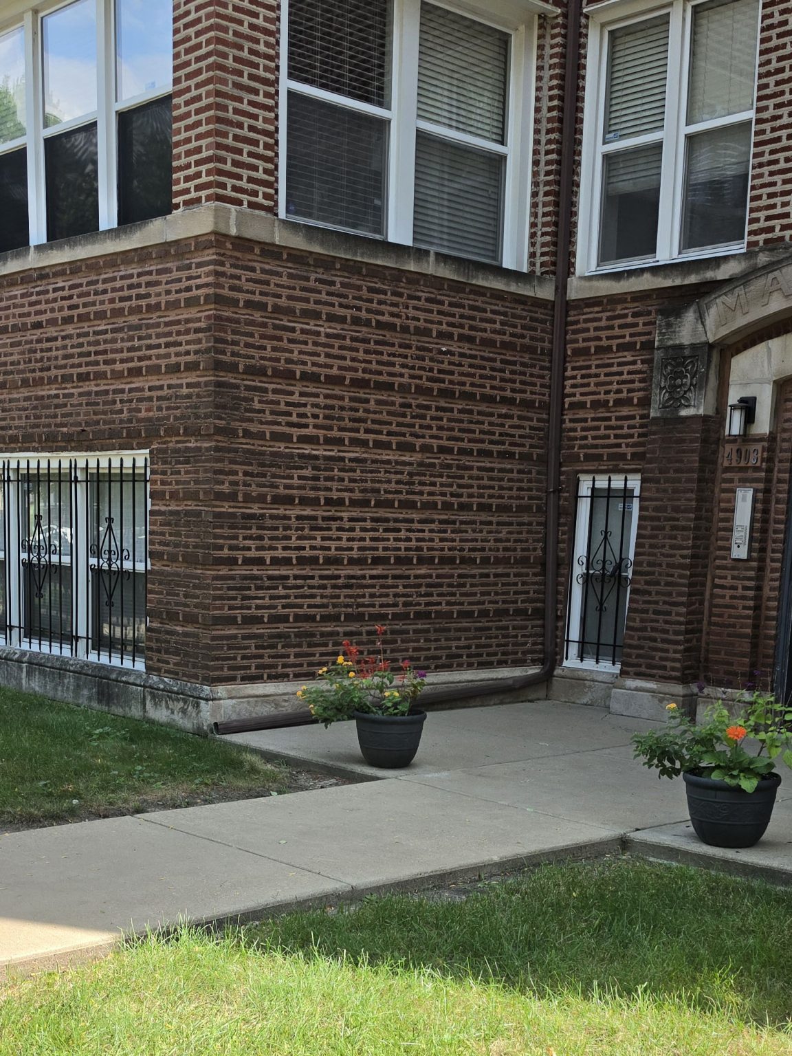 Brick multi-unit residential building in Albany Park, Chicago, with projecting bays, lower windows, masonry detailing, and a landscaped front setback.