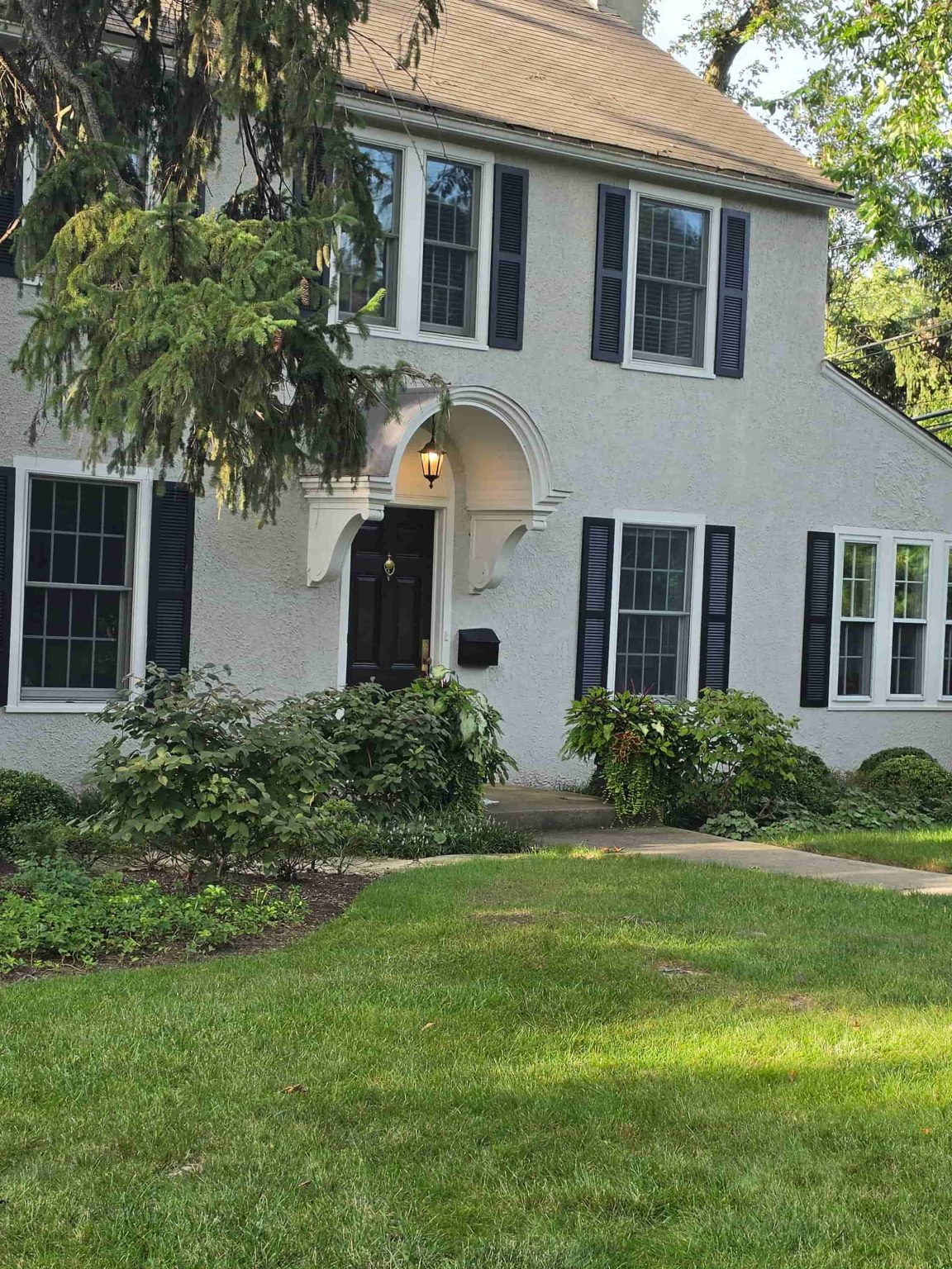 Stucco residence in Glencoe, Illinois, with an arched entry, mature trees, landscaped lawn, and traditional windows.