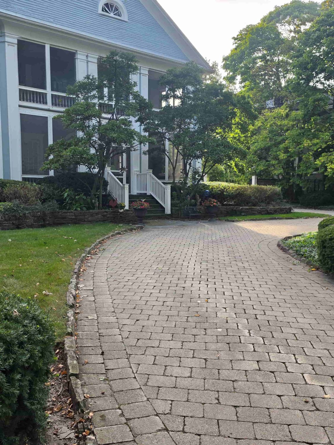 Two-story frame residence in Winnetka, Illinois, with a screened porch, mature landscaping, and a curved brick-paver drive.