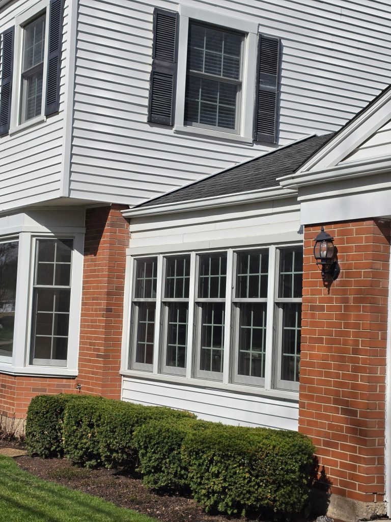 Sun-exposed house exterior with white siding, windows, brick walls, and garage