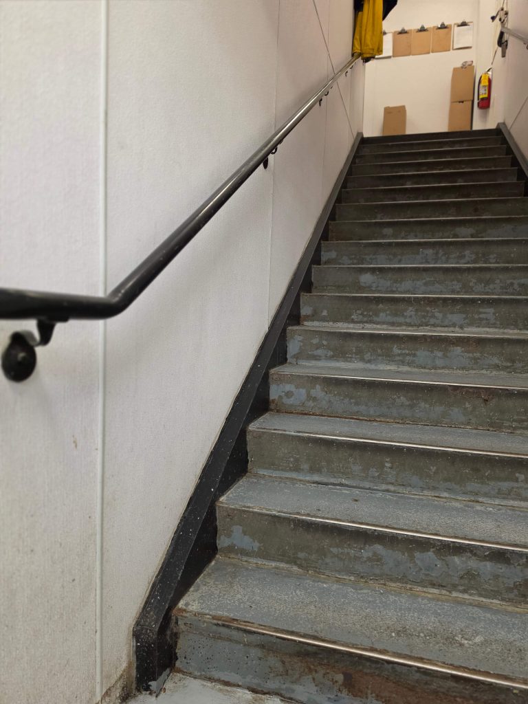 Worn painted service stairs with black handrail leading to an upper landing