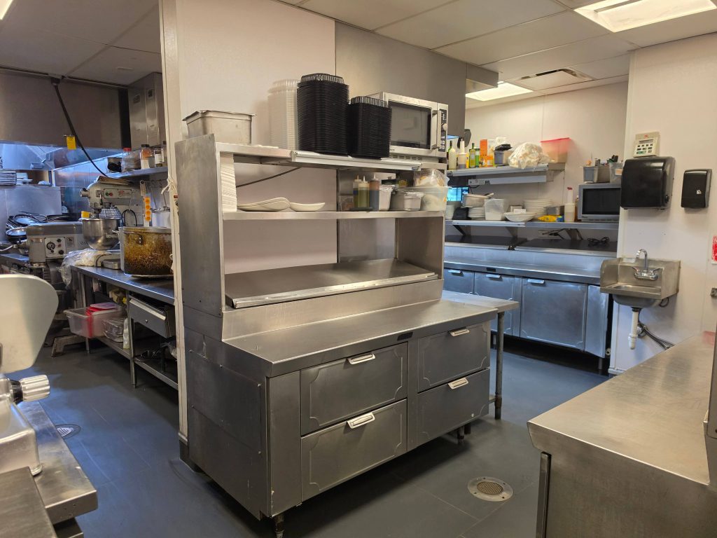 Commercial kitchen preparation room with stainless steel work island, shelves, and floor drain