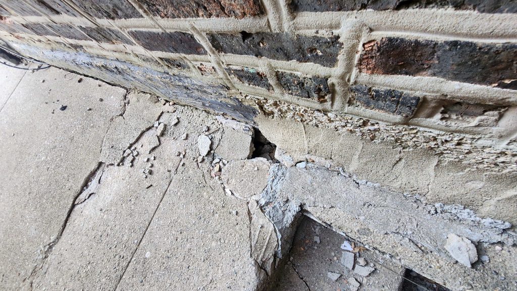 Cracked paving beside a brick wall.
