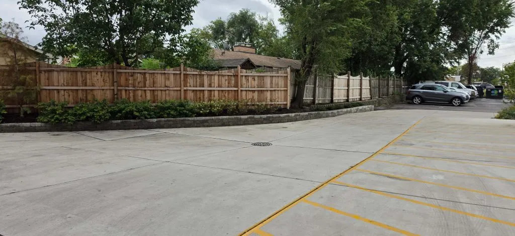 Wooden boundary fence and planting strip beside a parking area.
