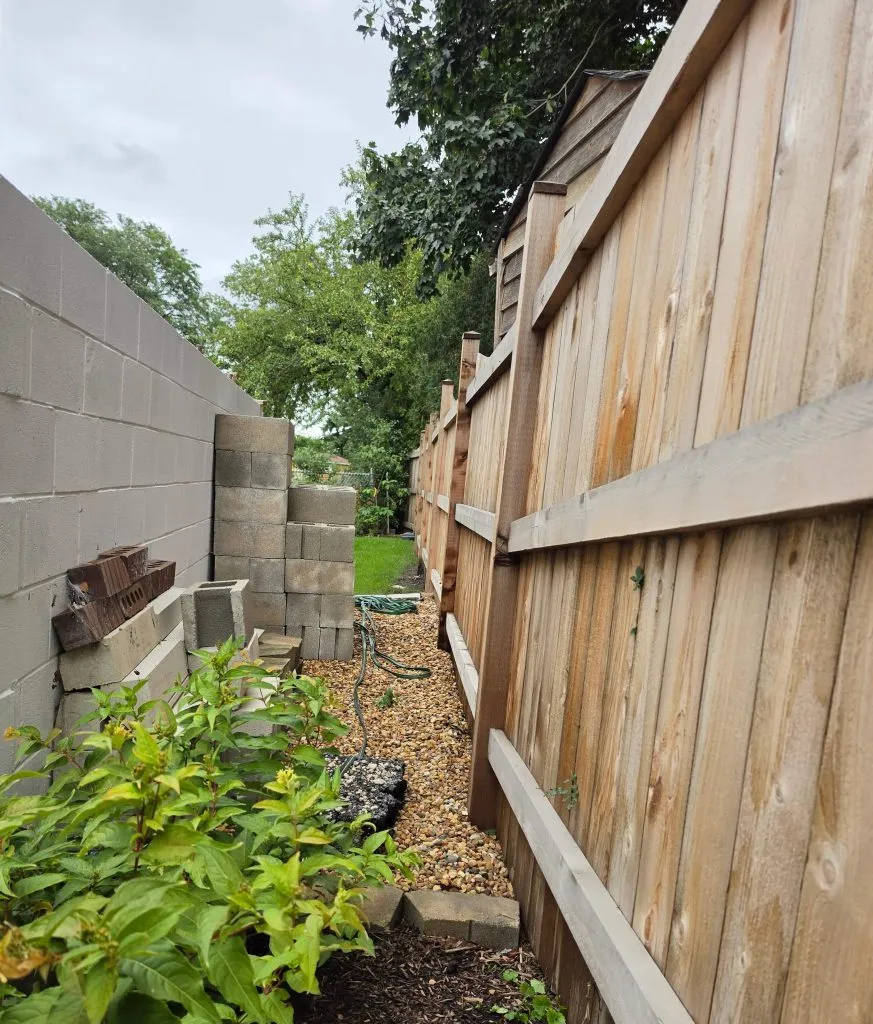 Stacked masonry in a passage between a block wall and wood fence.