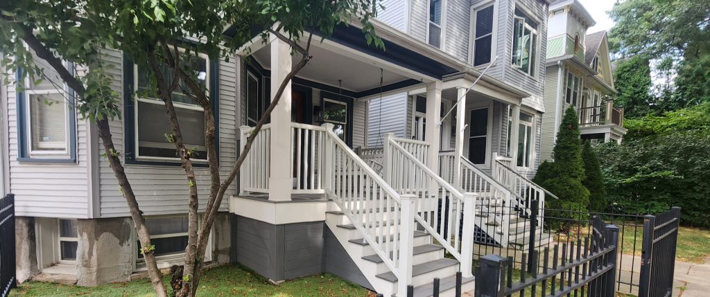 White front porch behind a garden and black fence.