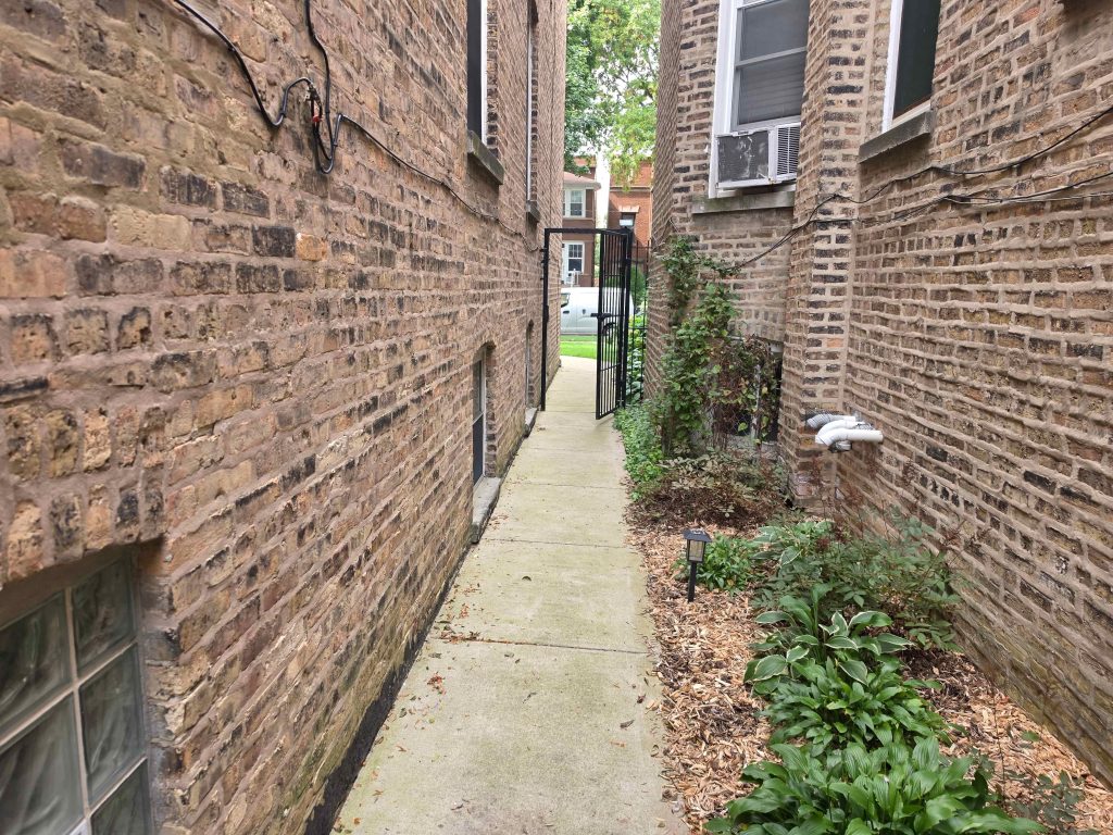 Narrow brick side passage with a planting strip and gate.