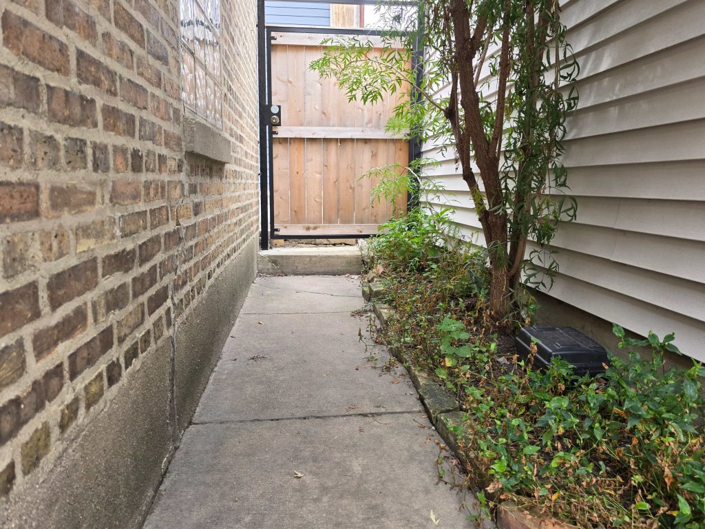 Narrow property passage with fencing and vegetation.