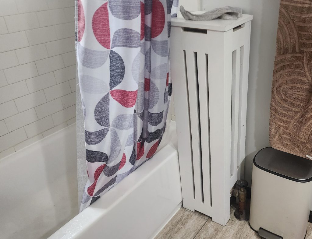 Covered radiator beside a bathtub.