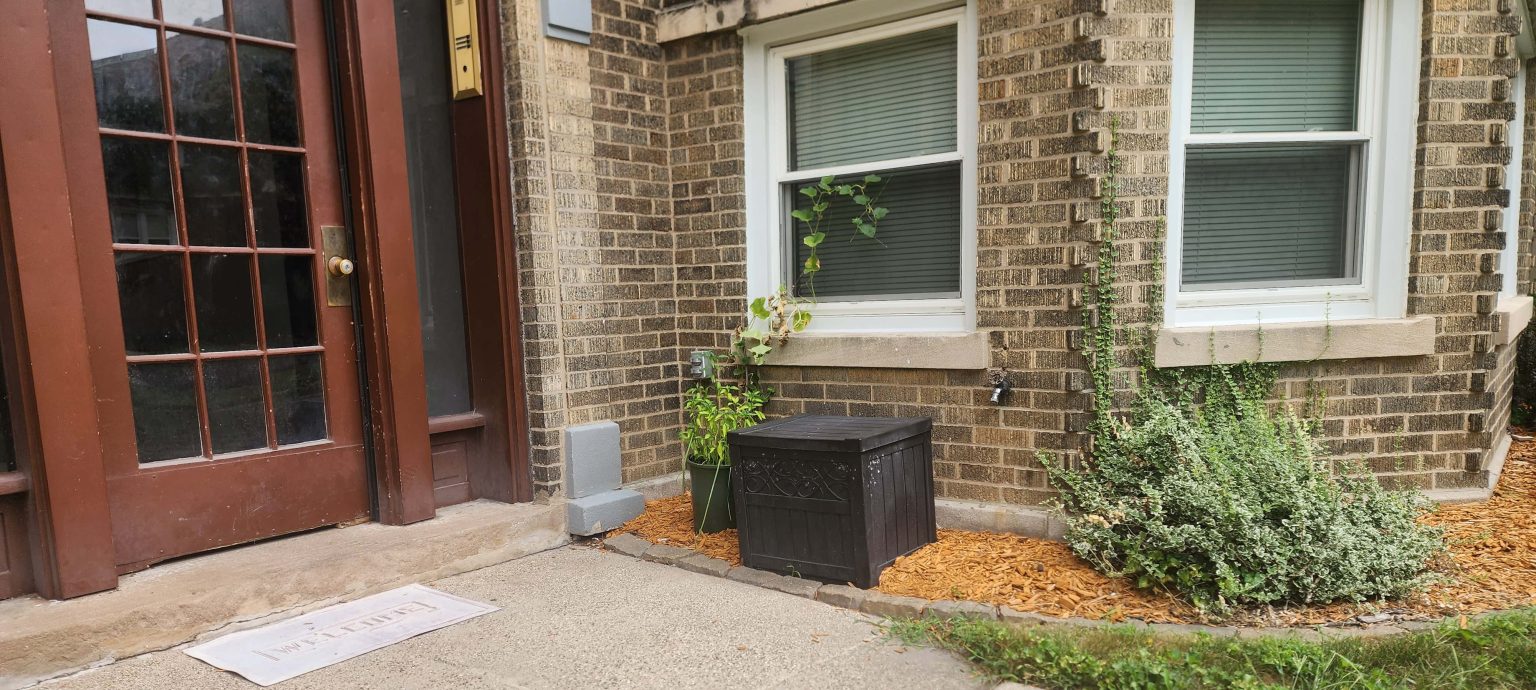 Brick entrance with windows, planting and a storage box.