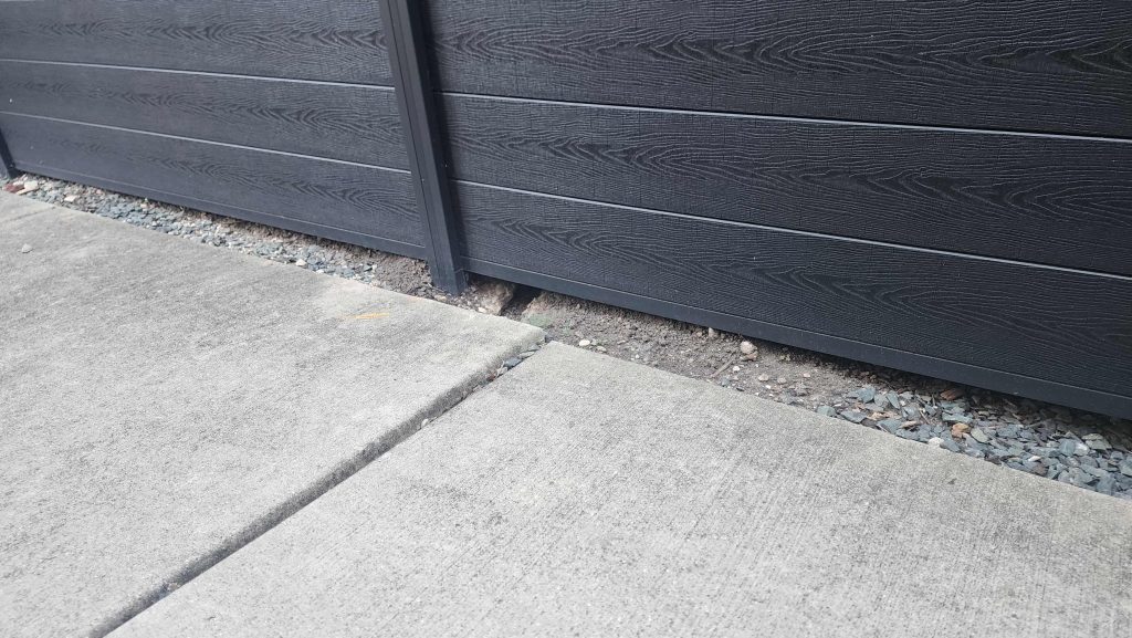 Fence base with gravel strip between horizontal fence boards and a concrete walkway