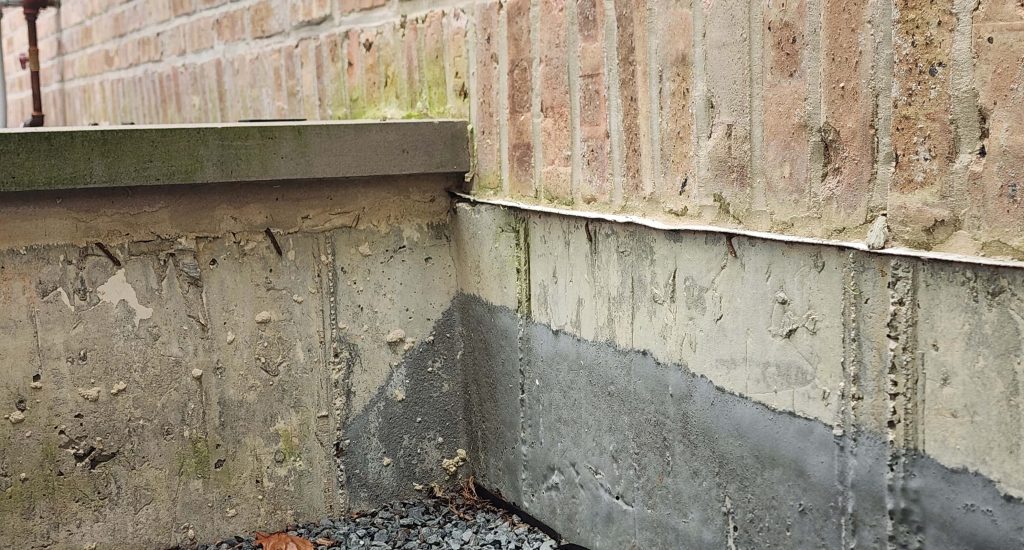 Brick wall meeting a gray foundation beside a retaining-wall cap.